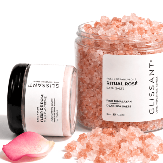 GLISSANT skincare set featuring a jar of Pink Himalayan Dead Sea Salts and a tube of Face & Mask Tallow Crème, with a pink rose petal on a clean white background.